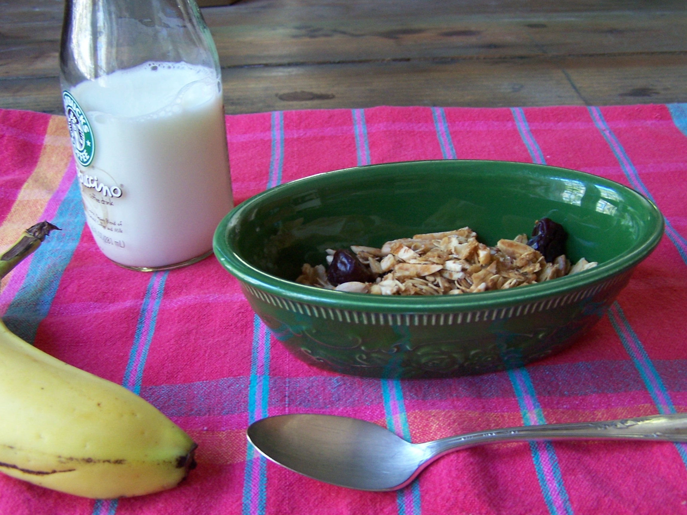 green bowl with granola, jar of milk, red towel, wood table