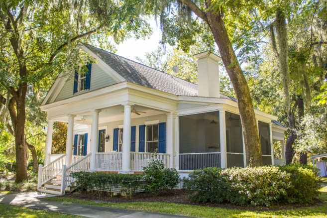house plan front/side view, front porch, side screened porch, chimney, light color home with blue shutters, wooded setting