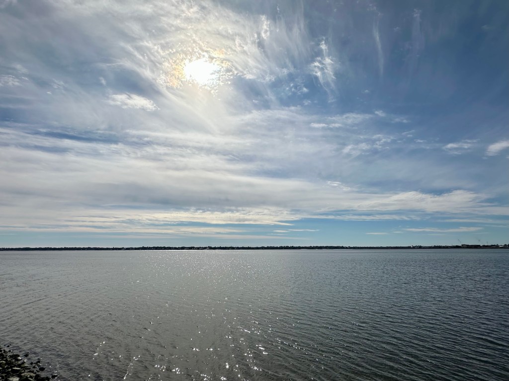 View from the battery in Charleston, SC, water with ripples, blue sky with clouds and sun, feel the sun