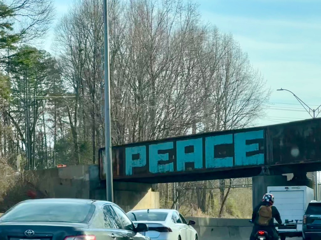 Dark overpass on busy highway with the word PEACE painted in blue, peace, signs, driving