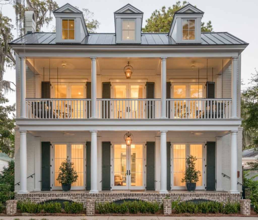 Exquisite home with two floors of French door, 3 French doors on each level, 3 dormers at the top, dusk, all lights on