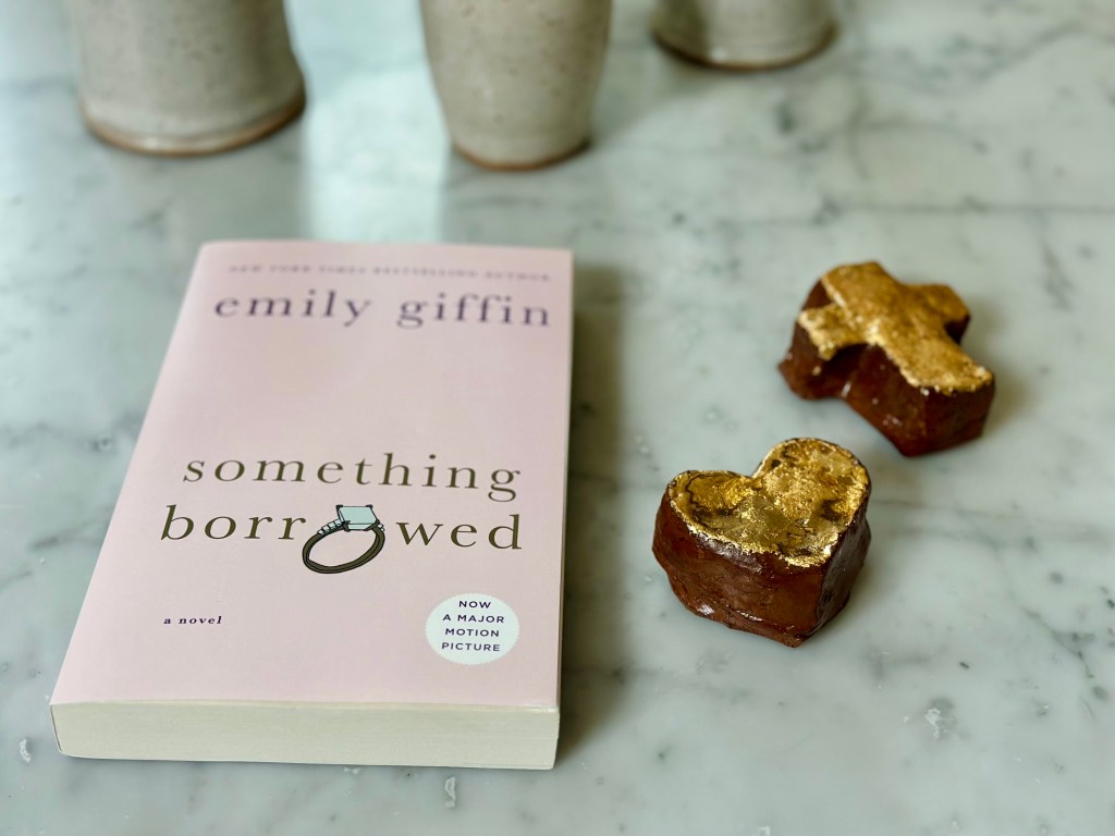marble table with light pink paperback book, cross, heart, something borrowed by Emily Giffin
