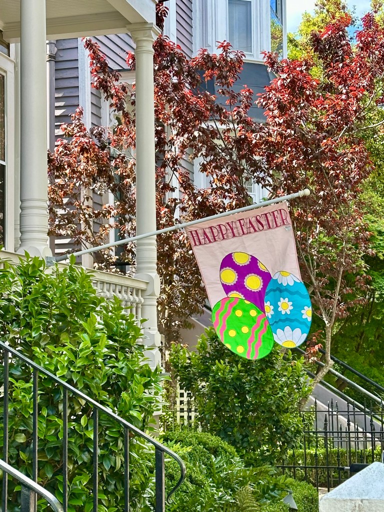 Front porch of home, flagpole, flag that reads Happy Easter, three brightly colored Easter eggs