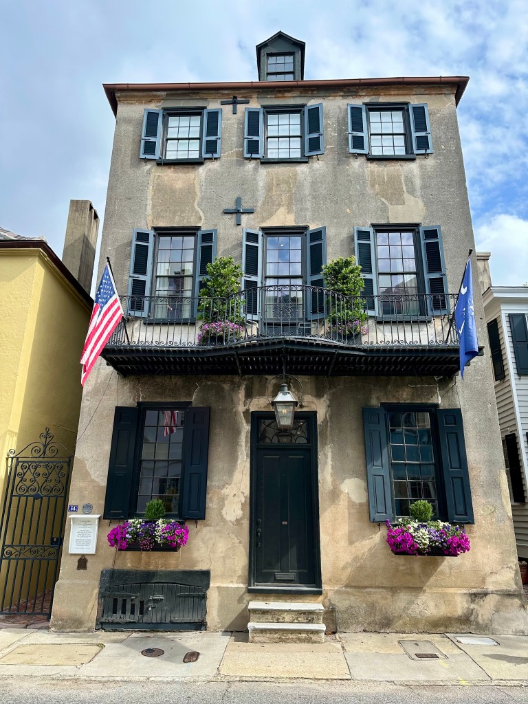 Historic home, with flags, hurricane bolts, worn patina, beautiful windows boxes with flower.