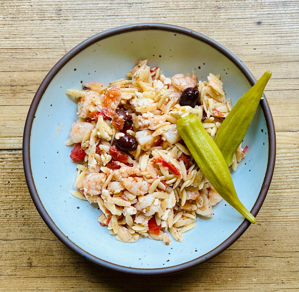 bowl with orzo salad with shrimp, tomatoes, olives and feta, pickled okra