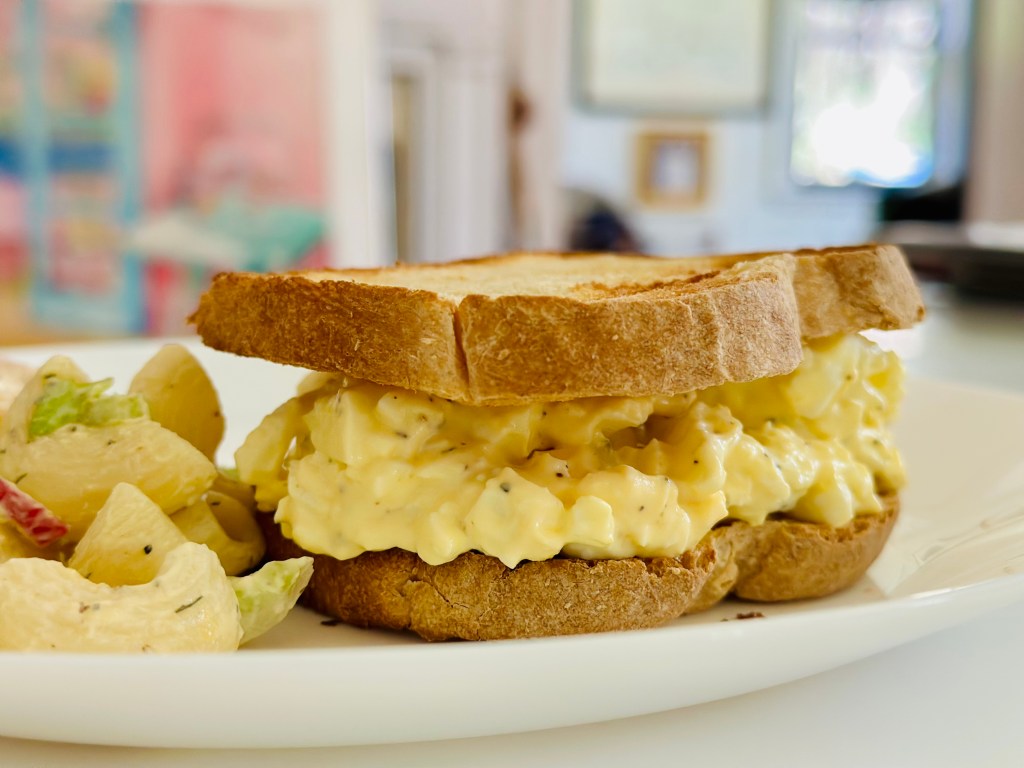 Egg salad sandwich, toast, egg salad, macaroni salad leftovers on white plate