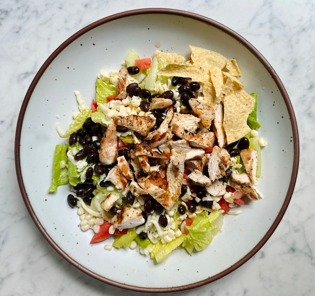 Salad with green lettuce, bits of grilled chicken, white corn, chopped tomato, black beans and pepper jack cheese