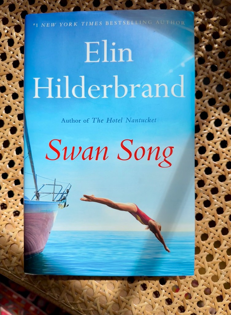 Book by Elin Hilderbrand, "Swan Song". Partial picture of sailboat with woman diving into water with red bathing suit on.