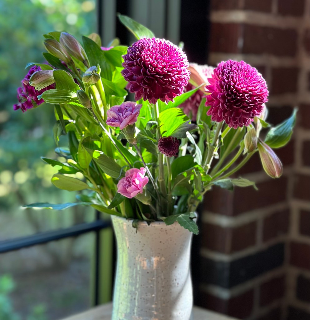 Vase with magenta color flowers on a table in the window.