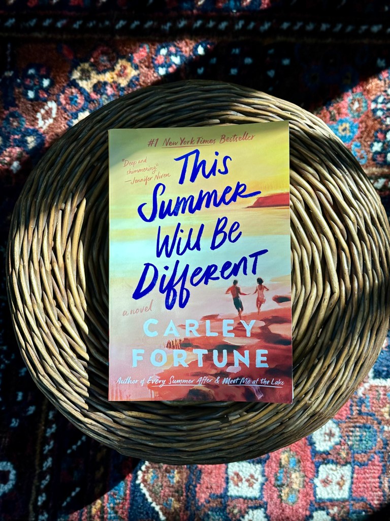 This Summer Will Be Different by Carley Fortune, book on a wicker stool on a rug.