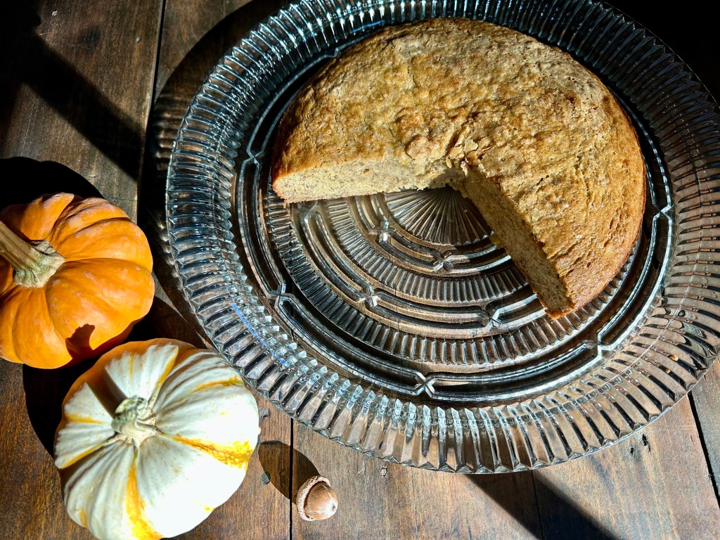 Joanna Gaines banana bread recipe baked and on a cake plate, two halloween gourds, rustic table, sunlight