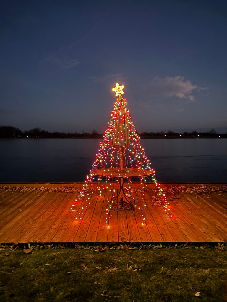 Christmas lights strung on an outdoor patio table. River background. Christmas tree appearance from a distance.