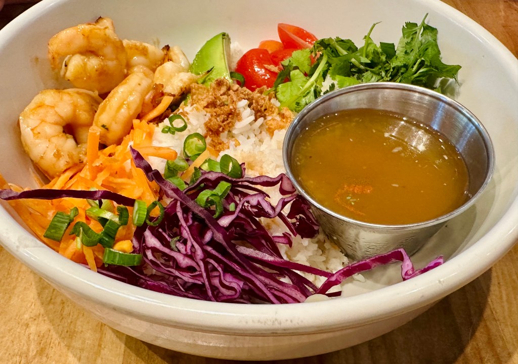 A bowl with rice, fresh veggies, herbs and shrimp.